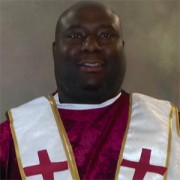 Large man in a red ministerial robe with a while stole trimmed in gold